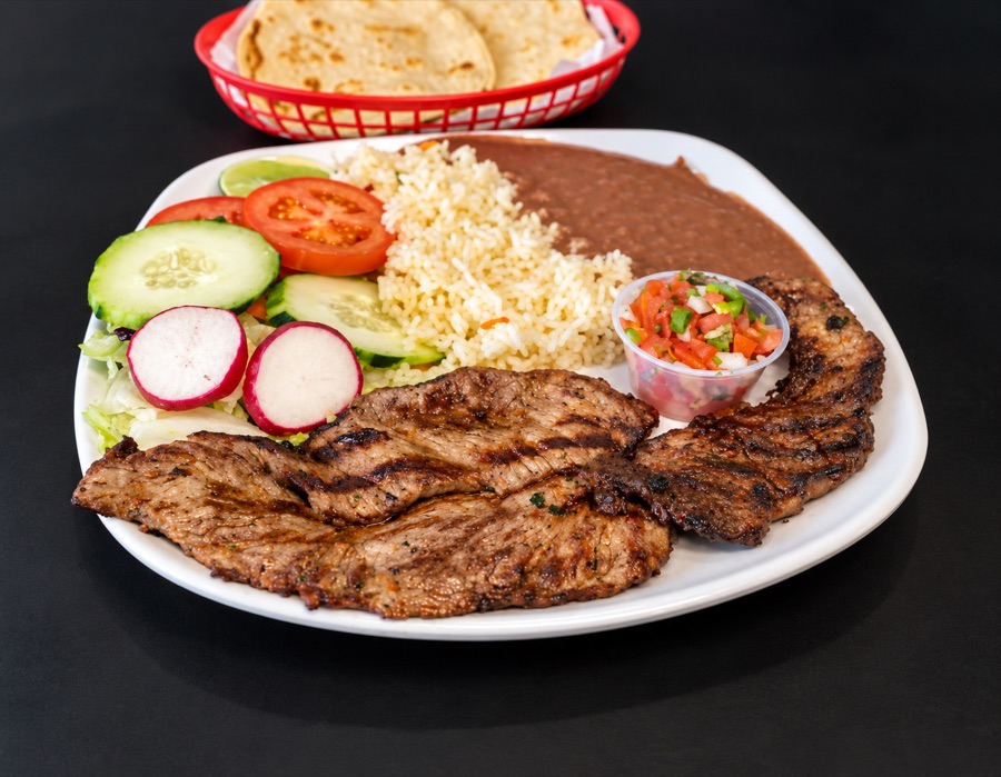 Grilled meat with rice, refried beans, salad and pico de gallo, tortillas in a red basket