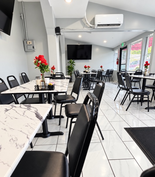 Dining room detail: marble tables set with red flowers and black chairs, the barred front windows in the background.
