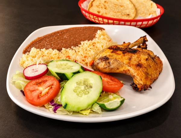 A roast chicken leg with rice, refried beans, salad and lime; tortillas in a red basket.
