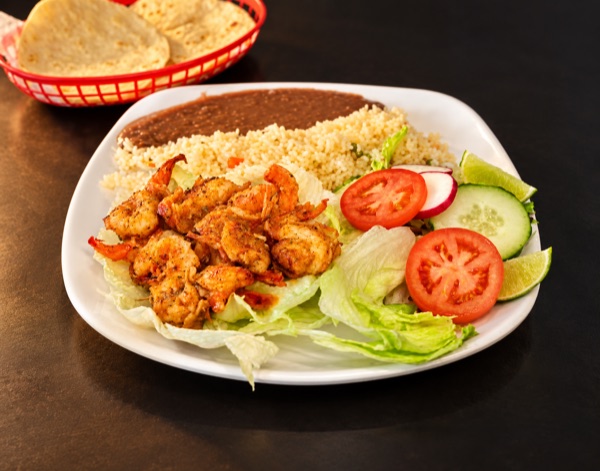 Seasoned shrimp over lettuce with rice, refried beans, tomato, cucumber and lime; tortillas in a red basket.