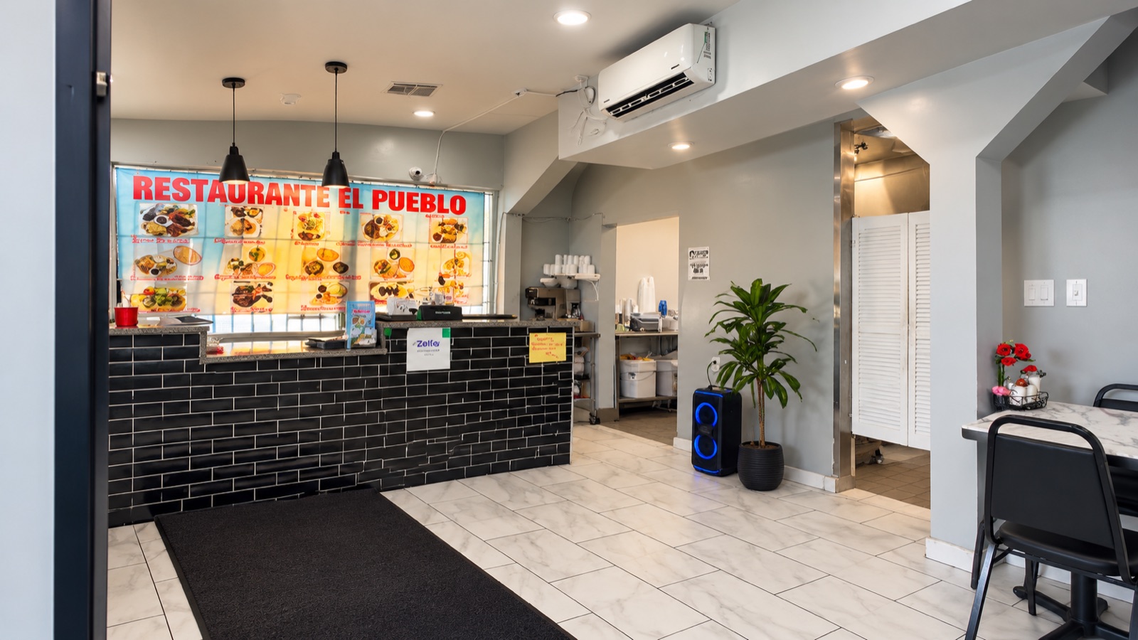 The order counter: black brick front, the backlit photo menu board, pendant lamps and the pass to the kitchen.